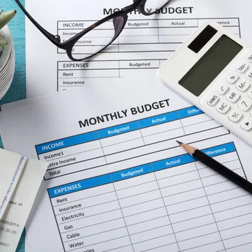 A picture of paper financial document with a pair of glasses, a pen and a calculator over them